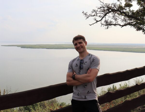 Młody mężczyzna uśmiecha się, w tle woda.